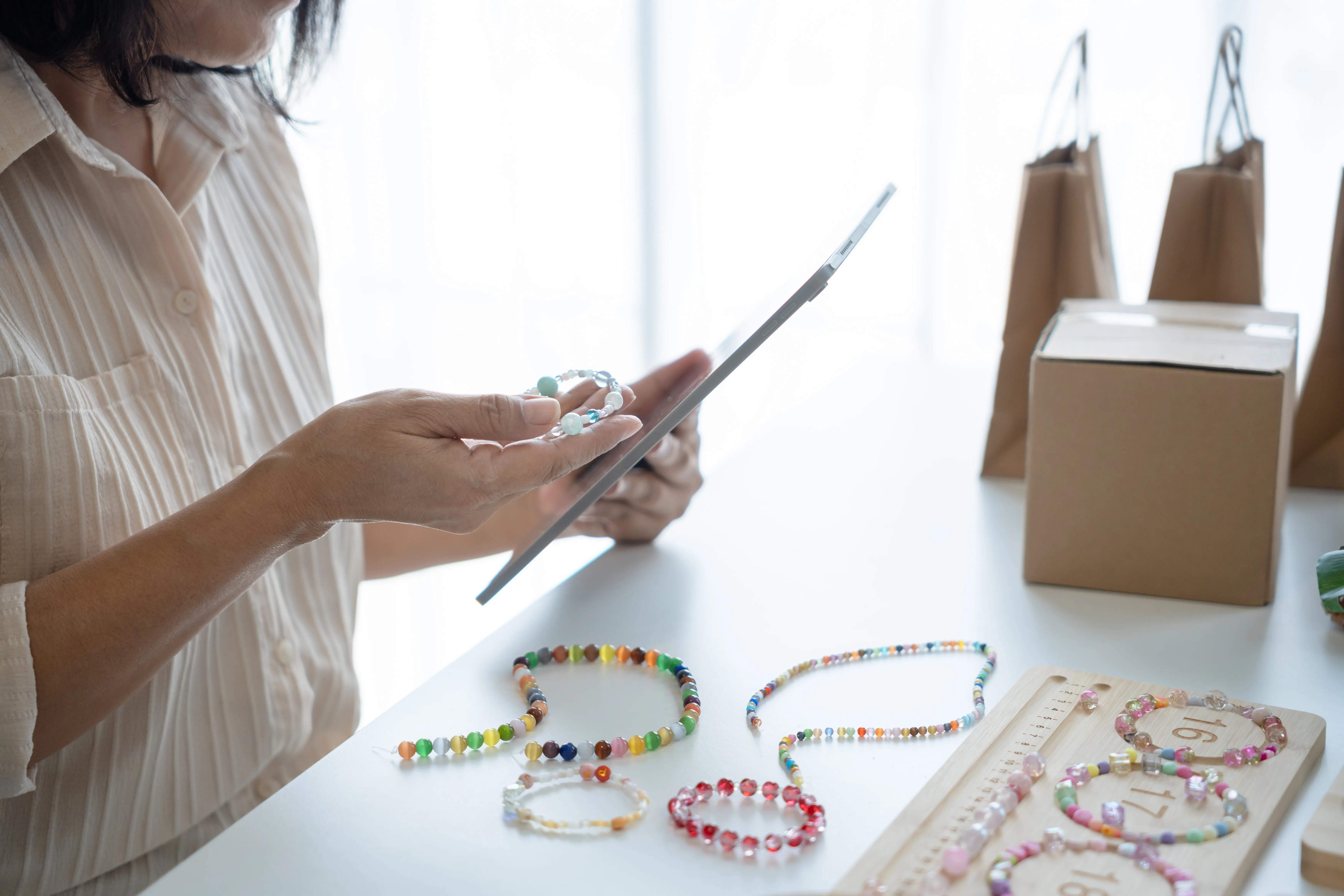 Reife asiatische Unternehmerin und Geschäftsinhaberin, E‑Commerce‑Onlinebestellungen mit Tablet, handgefertigte Schmuck‑Accessoires, Pappkarton.